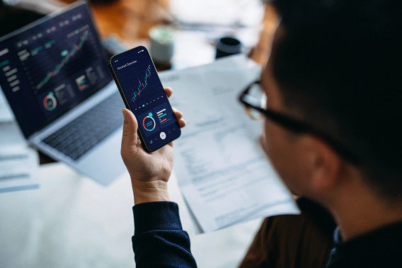 man holding phone with finance data on screen