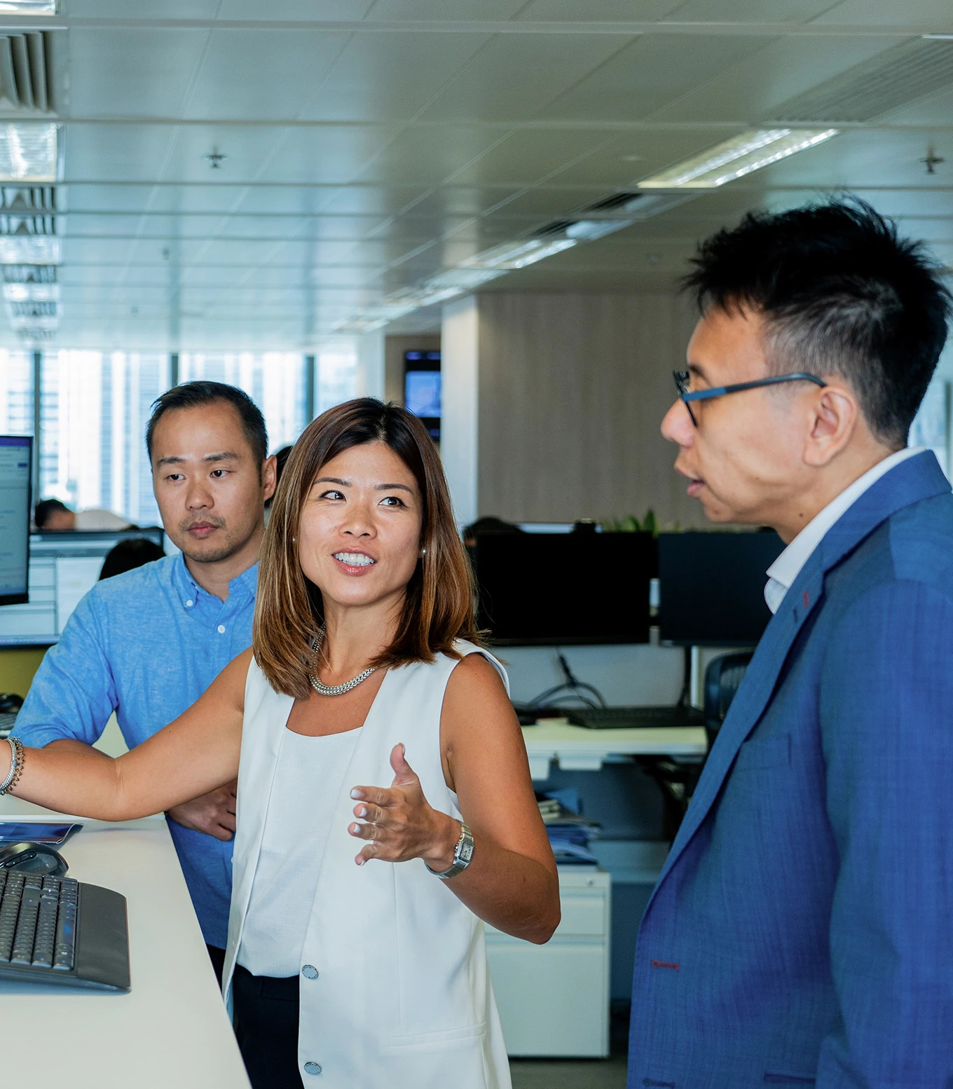 Three colleagues stood around one desk looking at the computer screen