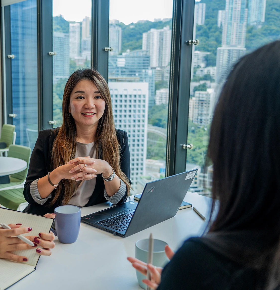 A smiling woman sat in a meeting area with two colleagues with her hands crossed