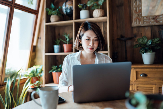 Young Asian woman working from home, video conferencing with business partners on laptop computer in home office.