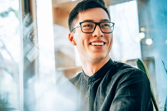 Asian male with glasses in black shirt, looking away from the camera smiling.